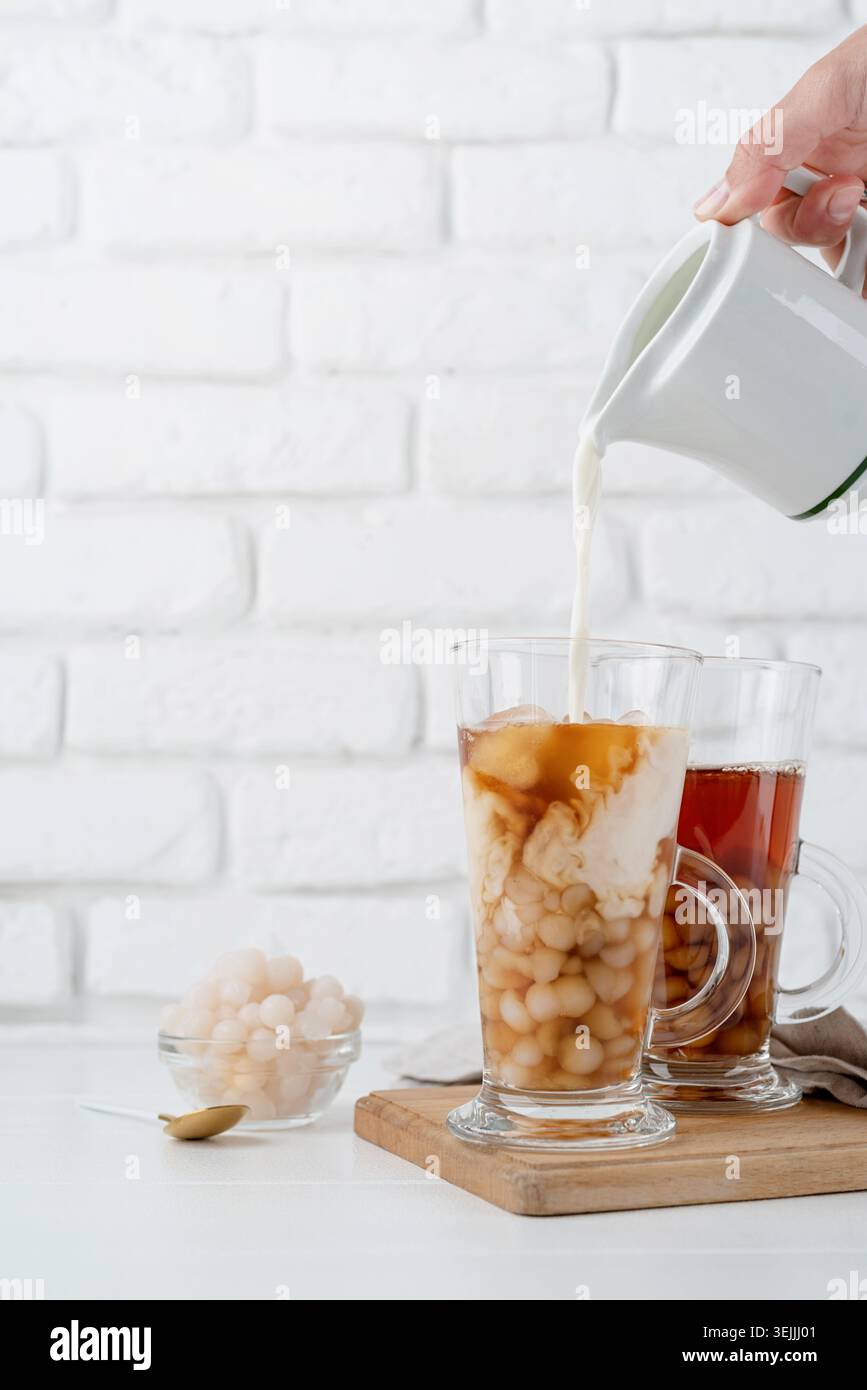Milch von Hand in Glas mit eisgekühltem Bubble Tee, weißem Backsteinhintergrund Stockfoto