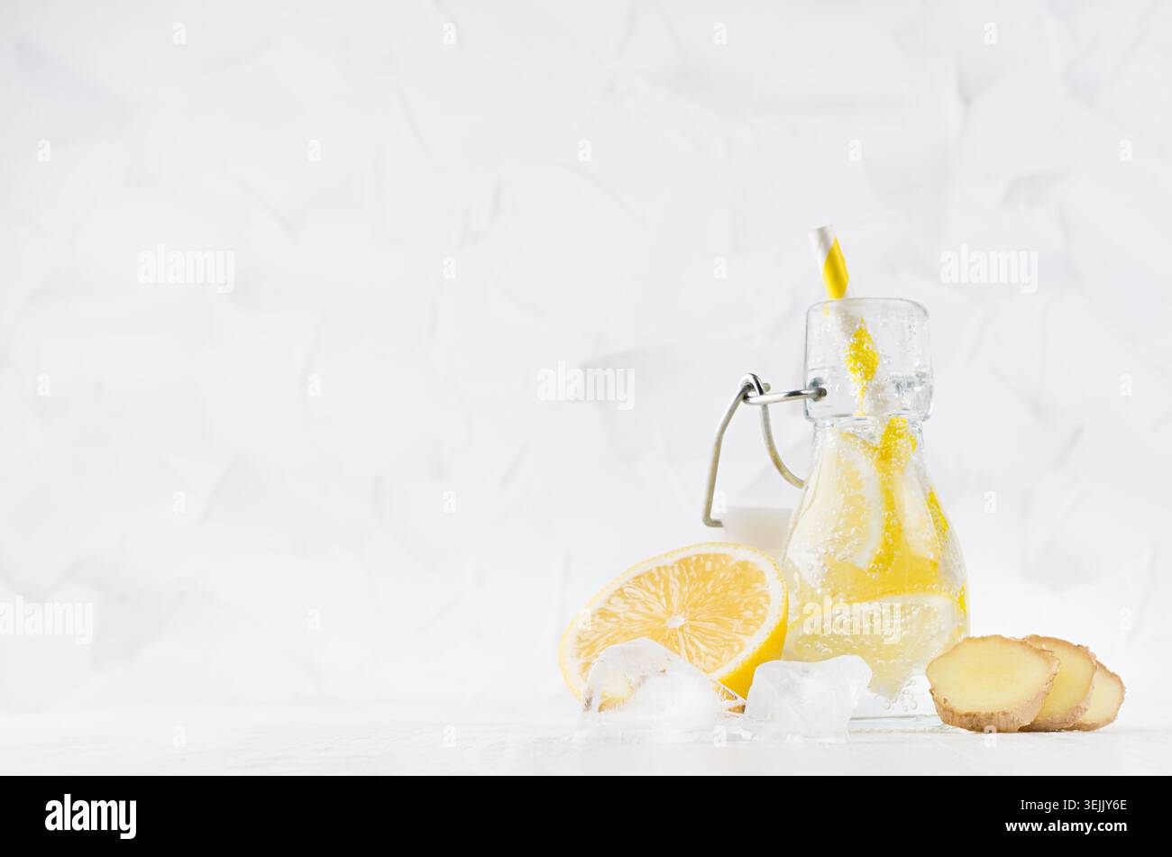 Erfrischendes kaltes Fruchtgetränk mit Zitrusfrucht, hellen Bläschen, Eis, Ingwer und Stroh in transparenter Passe in elegantem weiß Stockfoto
