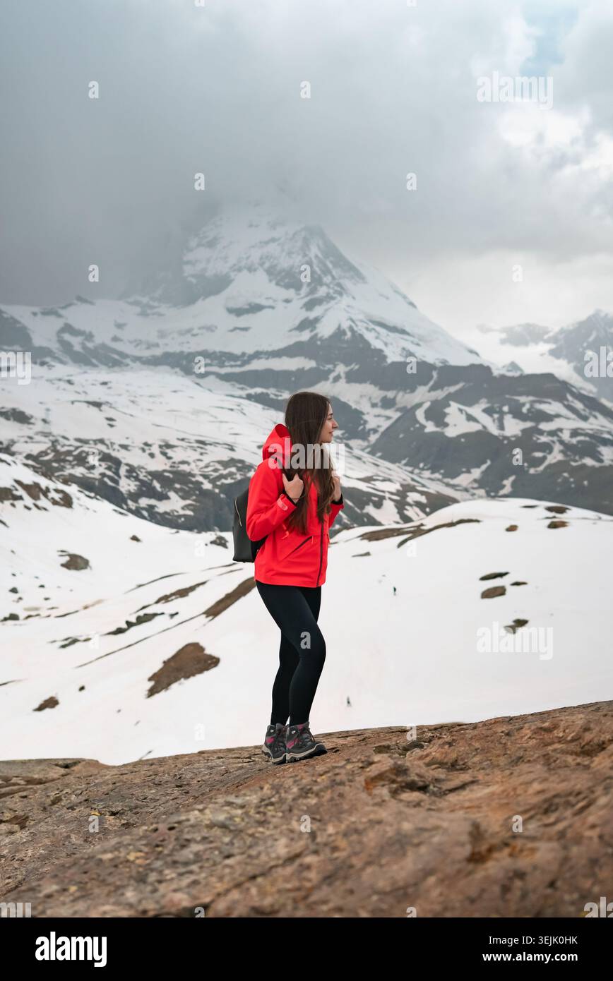 Frau, die auf Felsen steht und die schneebedeckte Berglandschaft unter bewölktem Himmel genießt Stockfoto