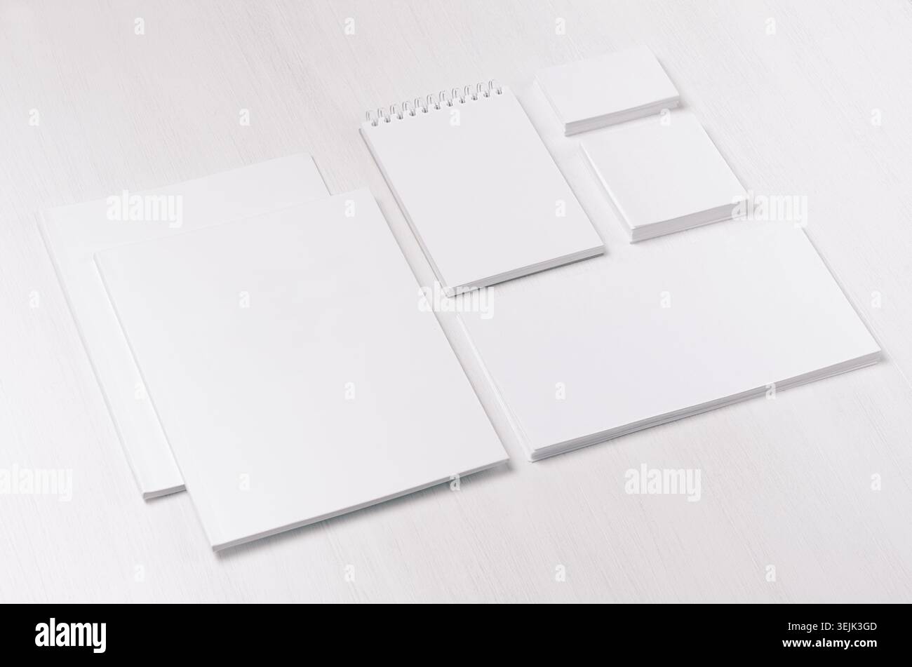 Weiße leere Visitenkarte, Umschlag, Broschüre, Notizblock, Aufkleber auf weicher weißer Holztafel, geneigt. Stockfoto