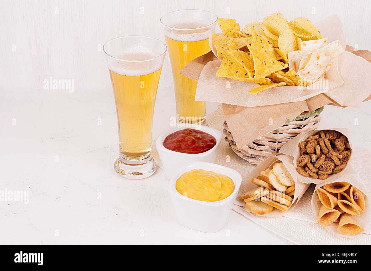 Verschiedene scharfe mexikanische Snacks und Saucen - Ketchup, Curry - in Schüssel, kaltes Lagerbier auf weißem Holzbrett. Stockfoto