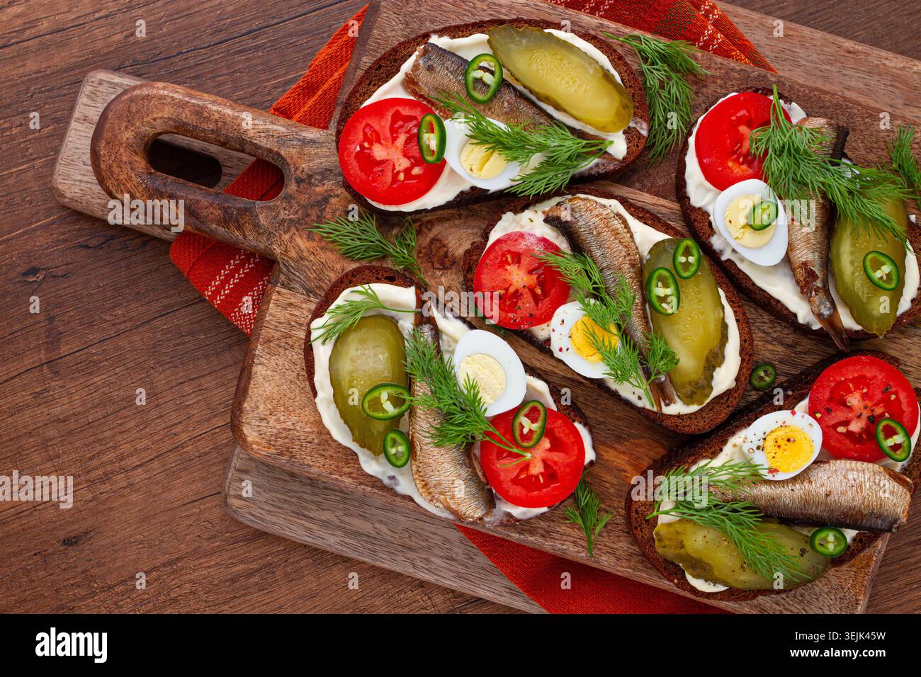 Offene Sandwiches mit Sprotten, Gemüse und Kräutern, auf Holzbrett, Frühstück, Snack, Stockfoto