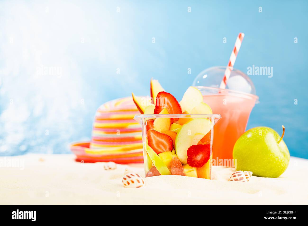 Heller Sommerfruchtsalat mit geschnittenen Früchten - Erdbeere, Mango, Grapefruit, Apfel in Plastikbox mit kaltem Saft, Sonnenhut auf Su Stockfoto