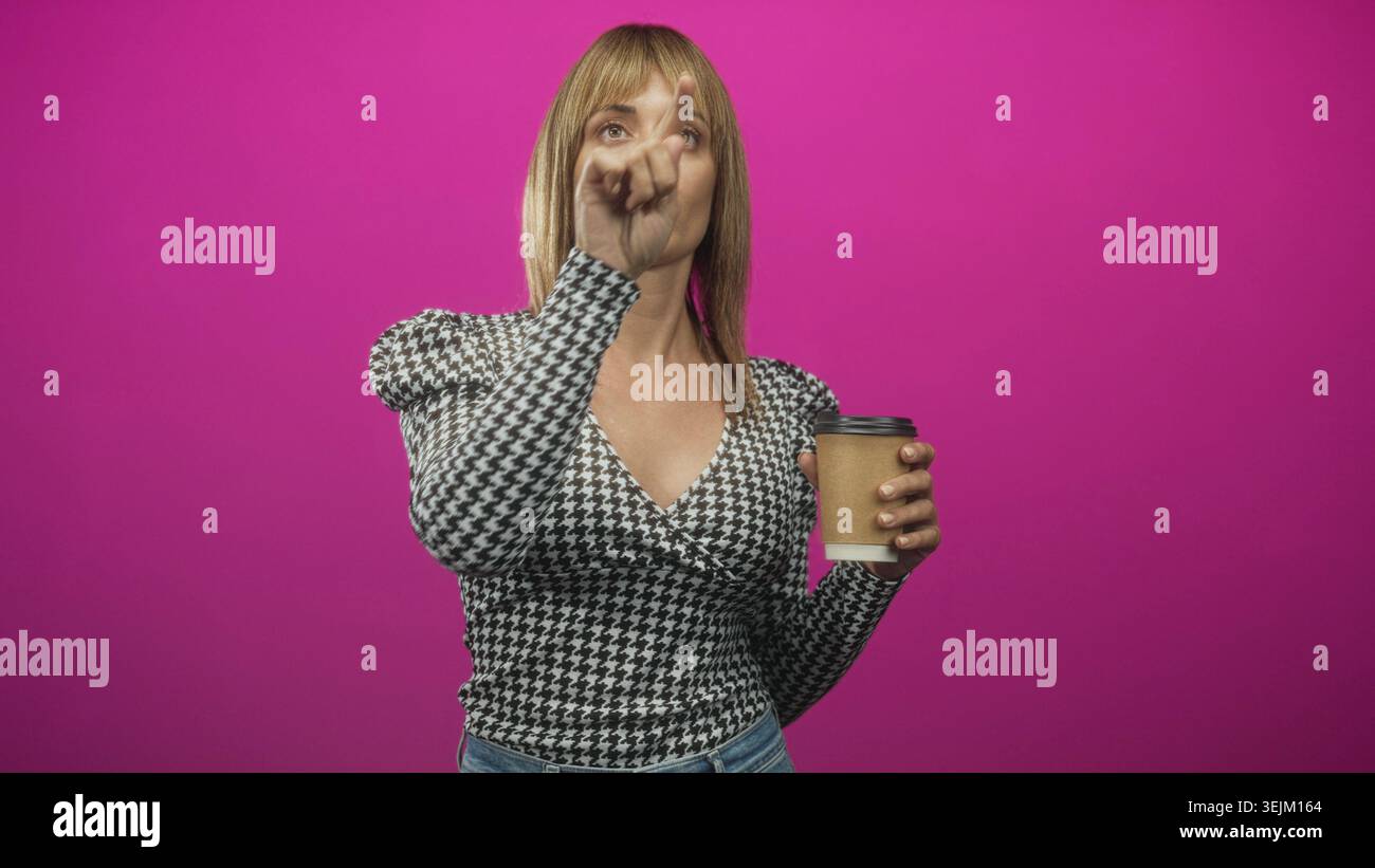Frau zeigt mit dem Zeigefinger, während sie die braune Kaffeetasse zum Mitnehmen hält und im Studio nach vorne blickt; Entschlossenheit. Stockfoto