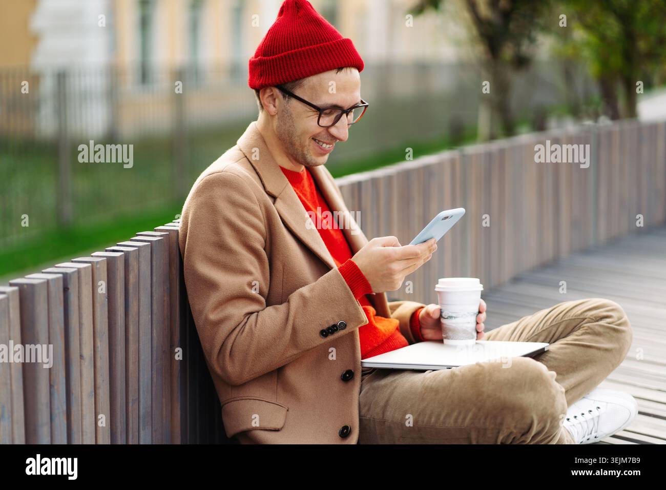 Hipster Mann mit Smartphone, chatten in sozialen Netzwerken, sitzen im Freien, trinken Kaffee oder Tee. Stockfoto