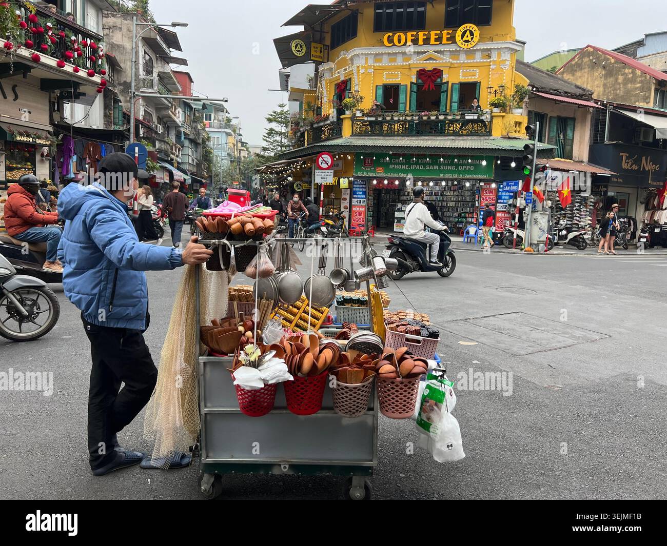Ein Straßenverkäufer schiebt einen Essenswagen mit Snacks und Eiern durch eine geschäftige Kreuzung in der Altstadt von Hanoi, Vietnam. - Smartphone-aufgenommenes Stockfoto