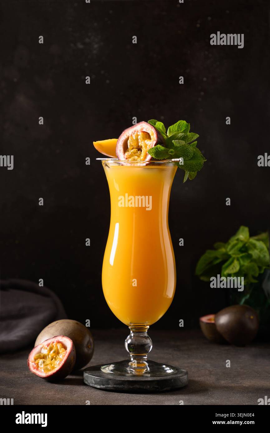 Passionsfrucht und Mangococktail oder Saft im Hurrikanglas auf Schwarz. Stockfoto