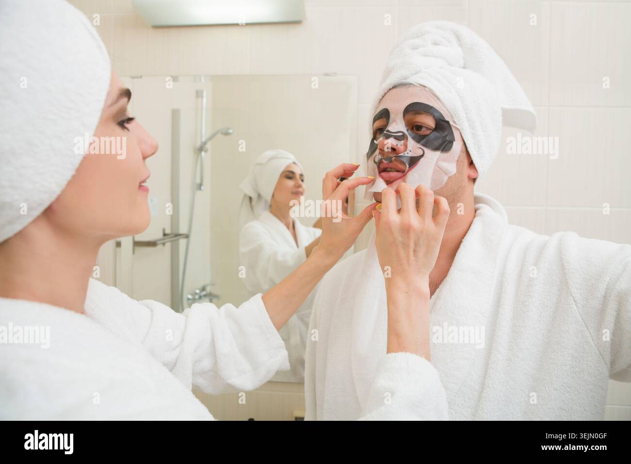 Junger Mann im weißen Morgenmantel, der sich mit Gesichtsmaske entspannt Stockfoto