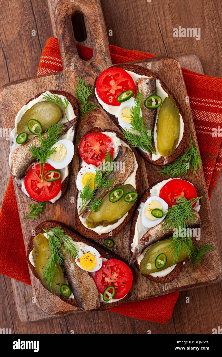 Offene Sandwiches mit Sprotten, Gemüse und Kräutern, auf Holzbrett, Frühstück, Snack, Stockfoto