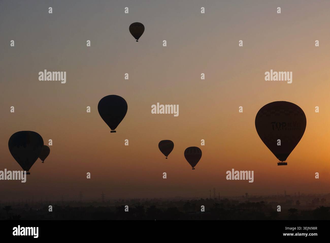 Mehrere Heißluftballons, die während des Sonnenaufgangs in der Nähe von Luxor, Ägypten, aufsteigen und eine atemberaubende Luftkulisse über der historischen Wüstenlandschaft schaffen. Stockfoto