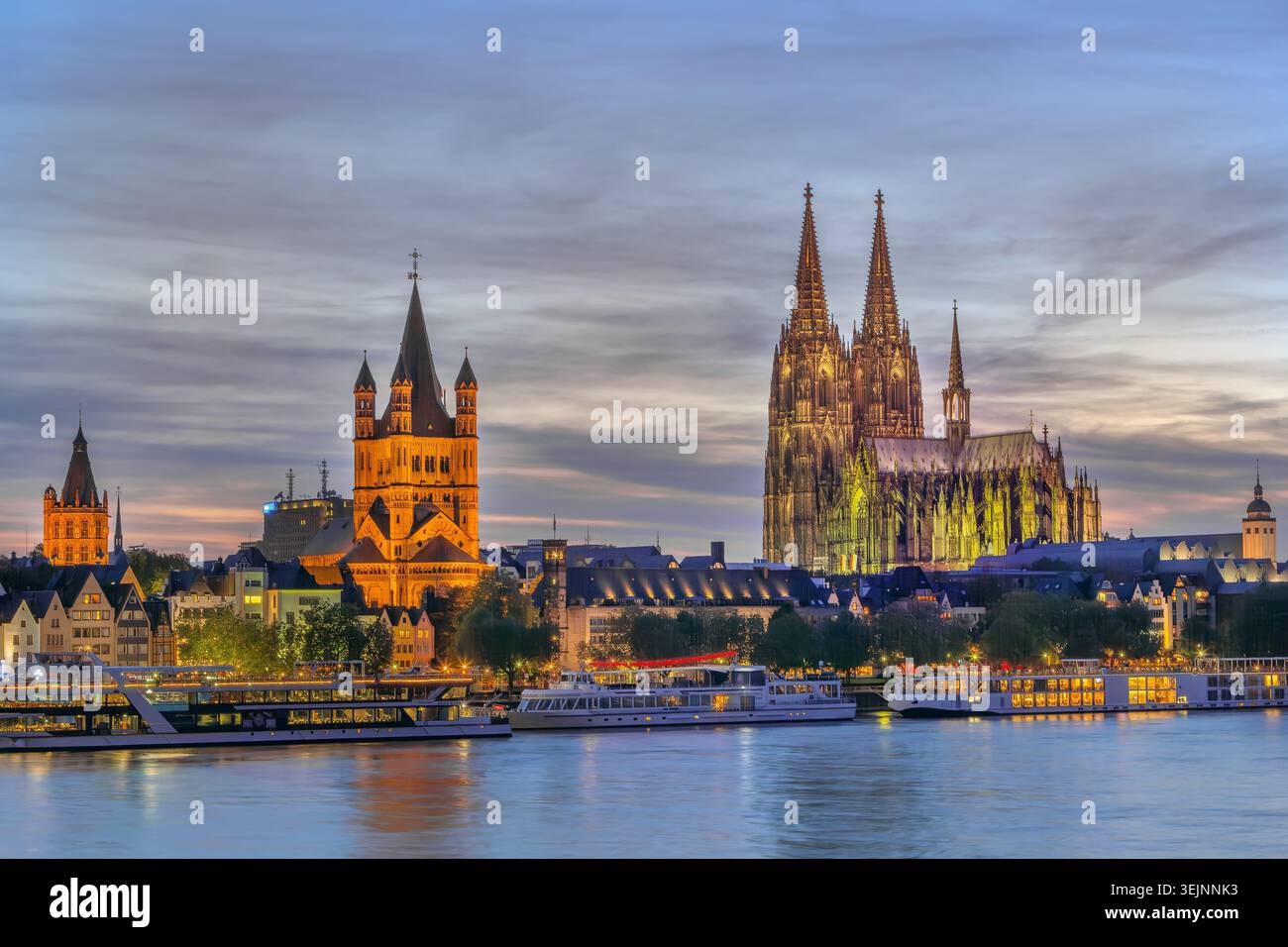 Kölns historisches Zentrum mit Blick auf den Dom und St. Martin am Abend vom Rhein in Deutschland. Beleuchtete Stadtarchitektur Stockfoto