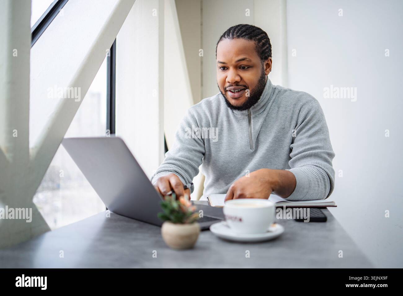 Junger schwarzer Mann, der im Café ferngesteuert am Laptop arbeitet Stockfoto