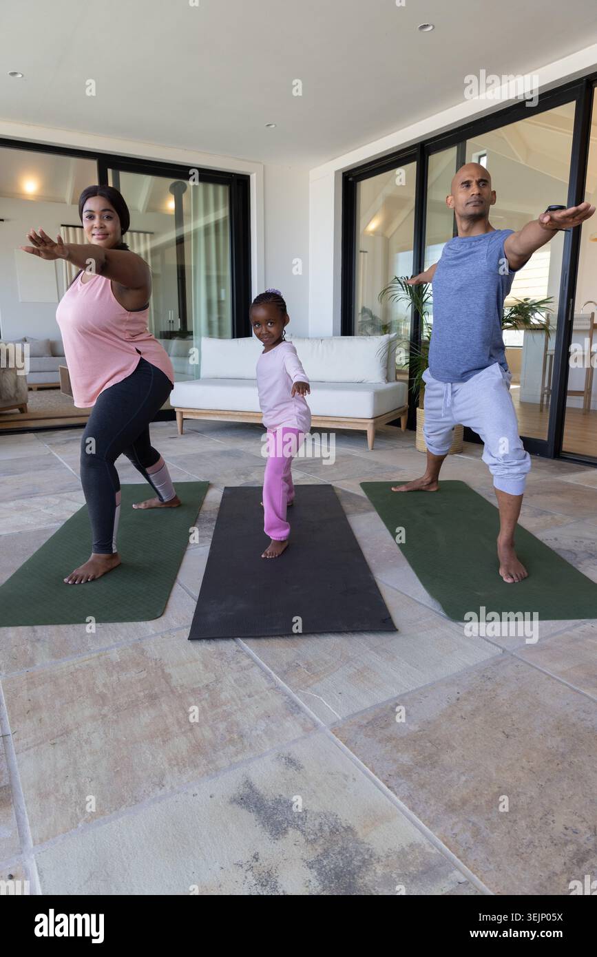 Afroamerikanische Familie in Activewear übt Yoga in gekachelten Sonnenzimmer auf zwei grünen, schwarzen Matten. Eltern, Kind, Terrasse, Glas, Stockfoto