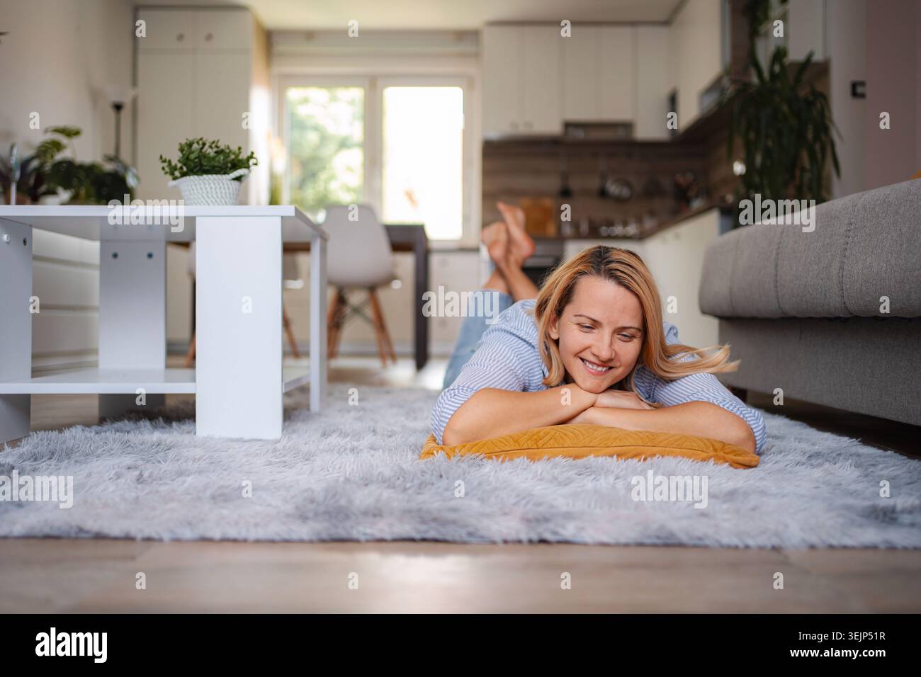 Frau, die sich auf dem Teppich im Wohnzimmer entspannt und das Wochenende genießt Stockfoto