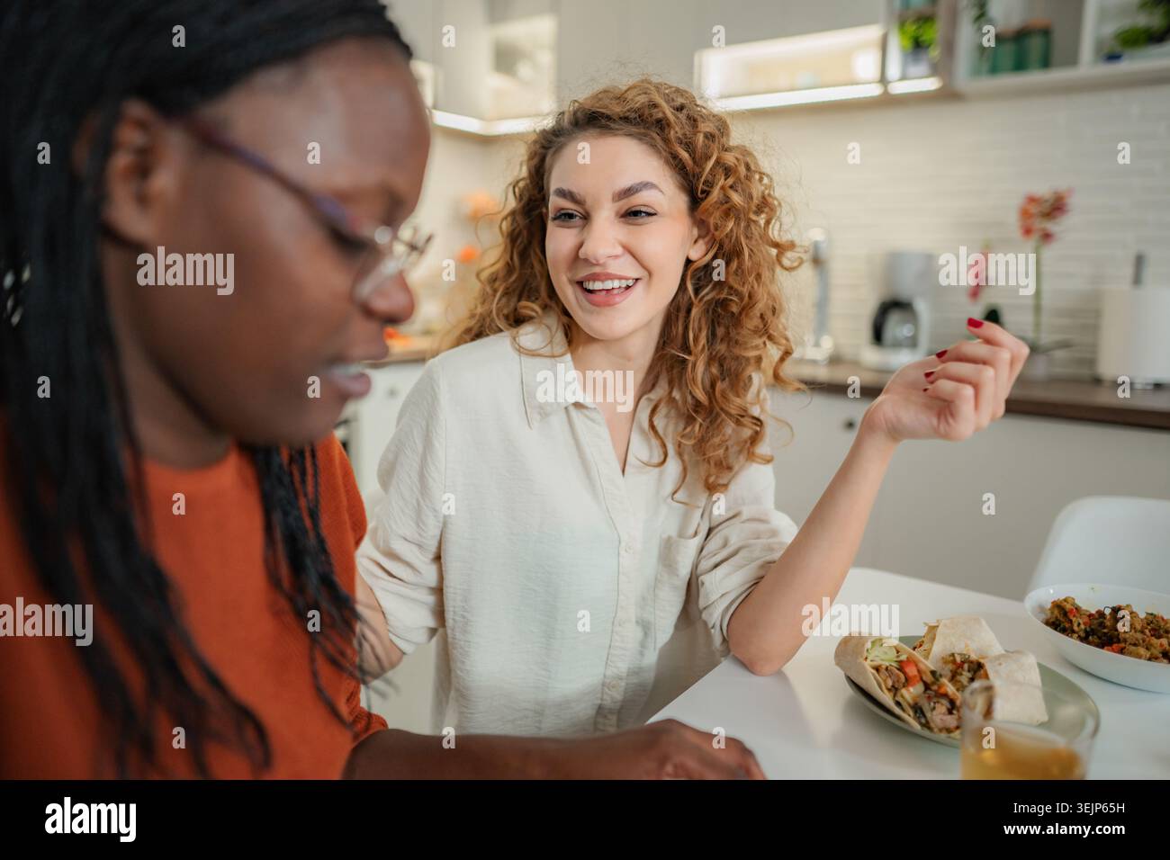 Verschiedene Freundinnen genießen Mittagessen und Gespräche in der Küche Stockfoto