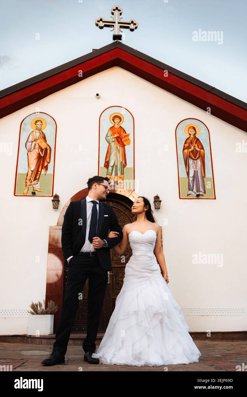 Braut und Bräutigam tauschen liebevolle Blicke auf die Kirche aus Stockfoto