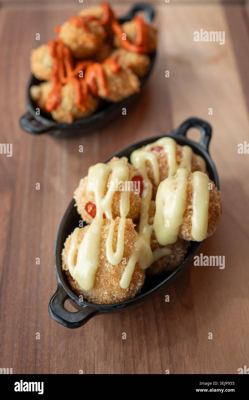 Knusprige Häppchen mit cremiger Sauce und lebhaftem Nieseln auf einem Holztisch Stockfoto