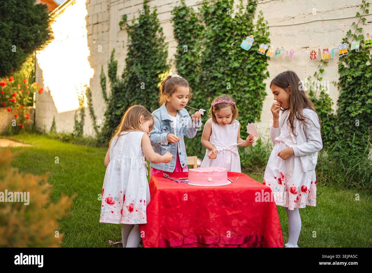 Kinder genießen die Kuchenfeier in sonnigem Garten Stockfoto