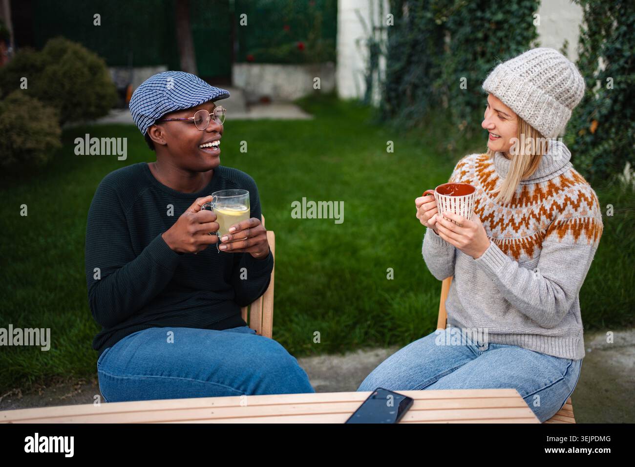 Verschiedene weibliche Freunde genießen heiße Getränke im Freien und lachen Stockfoto