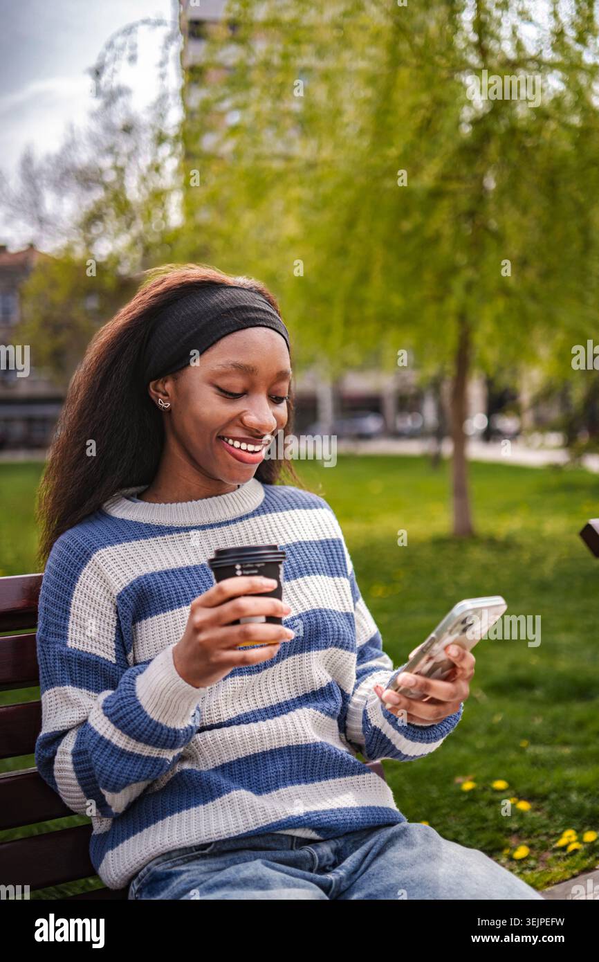 Frau genießt Kaffeepause im Park mit Smartphone Stockfoto