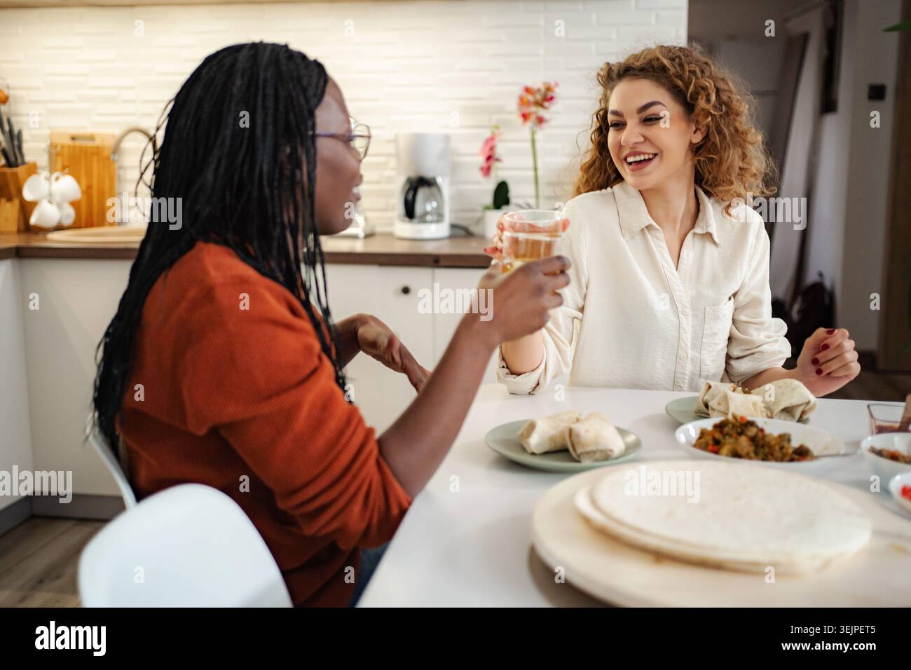 Verschiedene Freunde genießen Essen und unterhalten sich in der Küche Stockfoto
