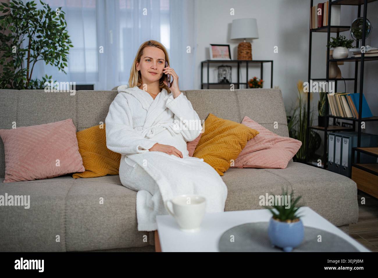 Frau, die auf dem Smartphone im Bademantel spricht und sich zu Hause auf der Couch entspannt Stockfoto