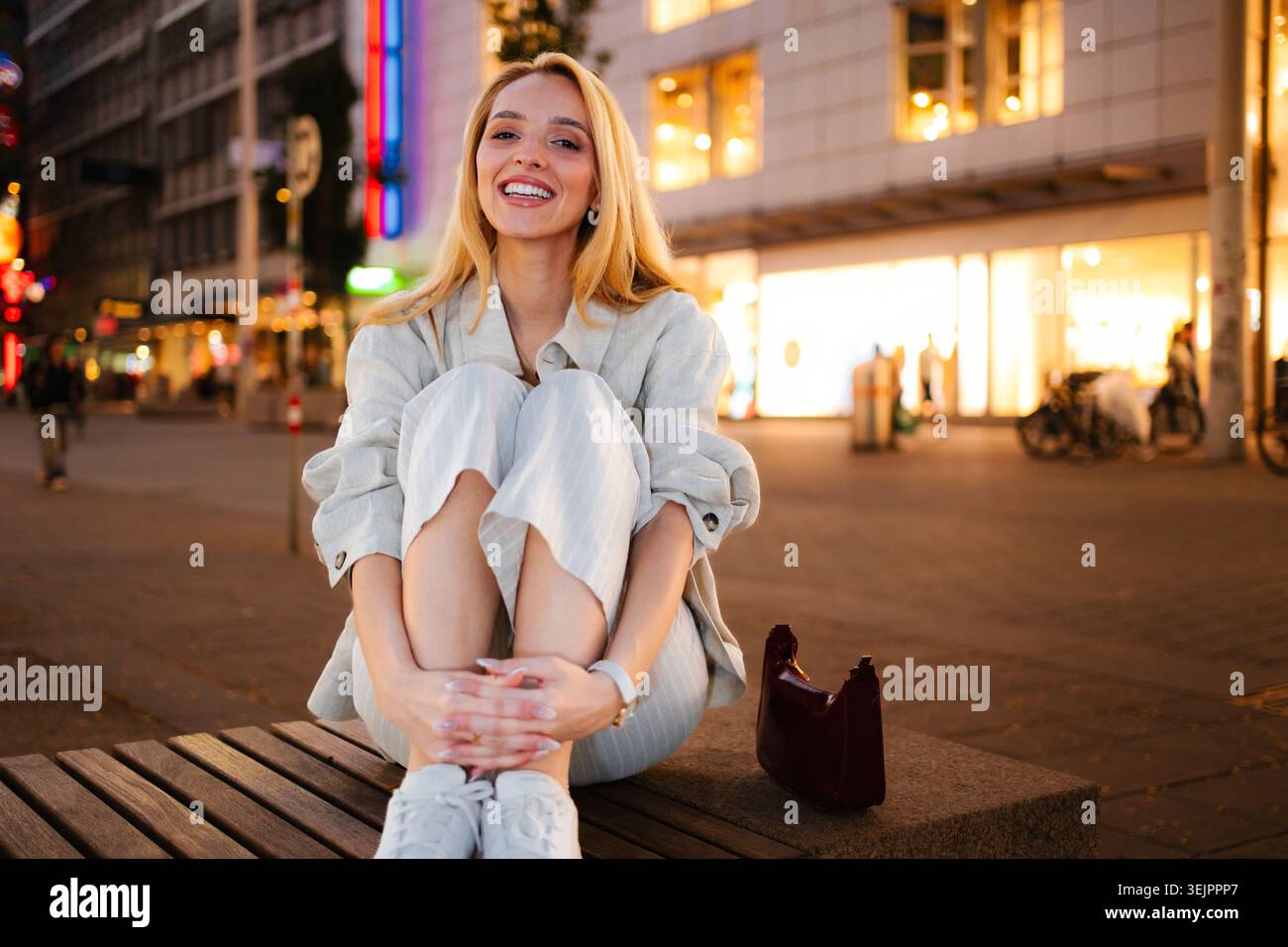 Glückliche junge Frau, die nachts in Wien auf der Bank sitzt Stockfoto