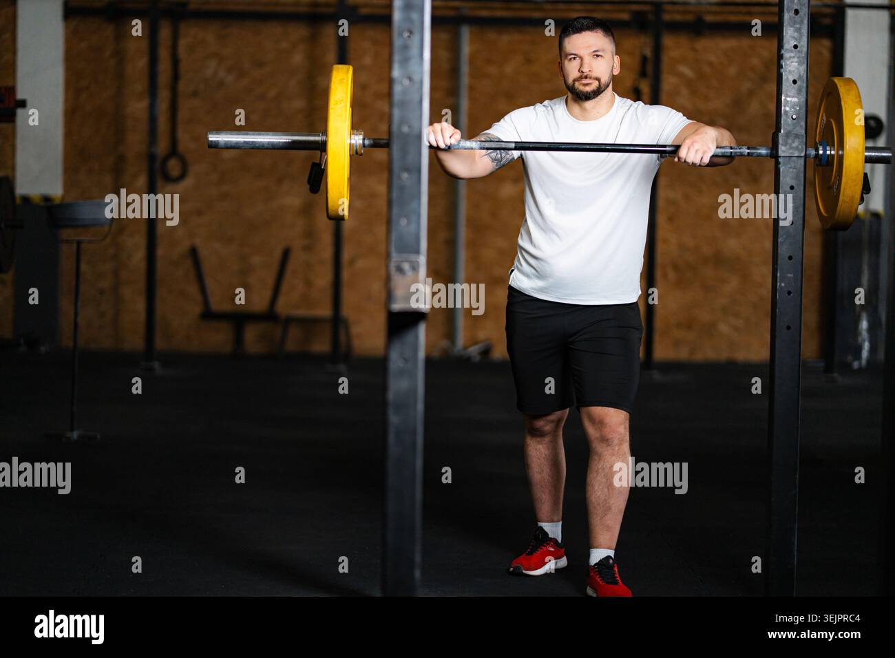 Mann, der auf Langhantel im Hockgestell im Fitnessstudio ruht Stockfoto