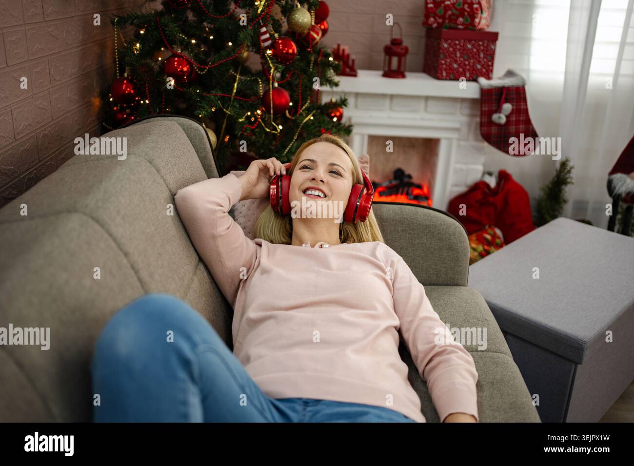 Am gemütlichen Weihnachtsfeuer entspannt eine junge Frau ihre Lieblingsmusik, während sie den festlichen Geist liebt Stockfoto