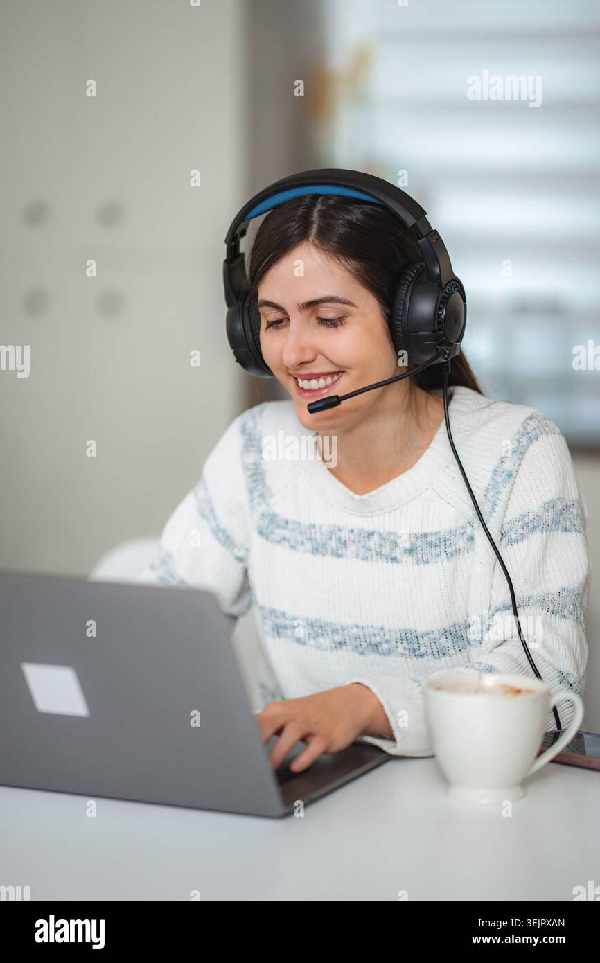 Frau mit Headset, die von zu Hause aus am Laptop arbeitet Stockfoto
