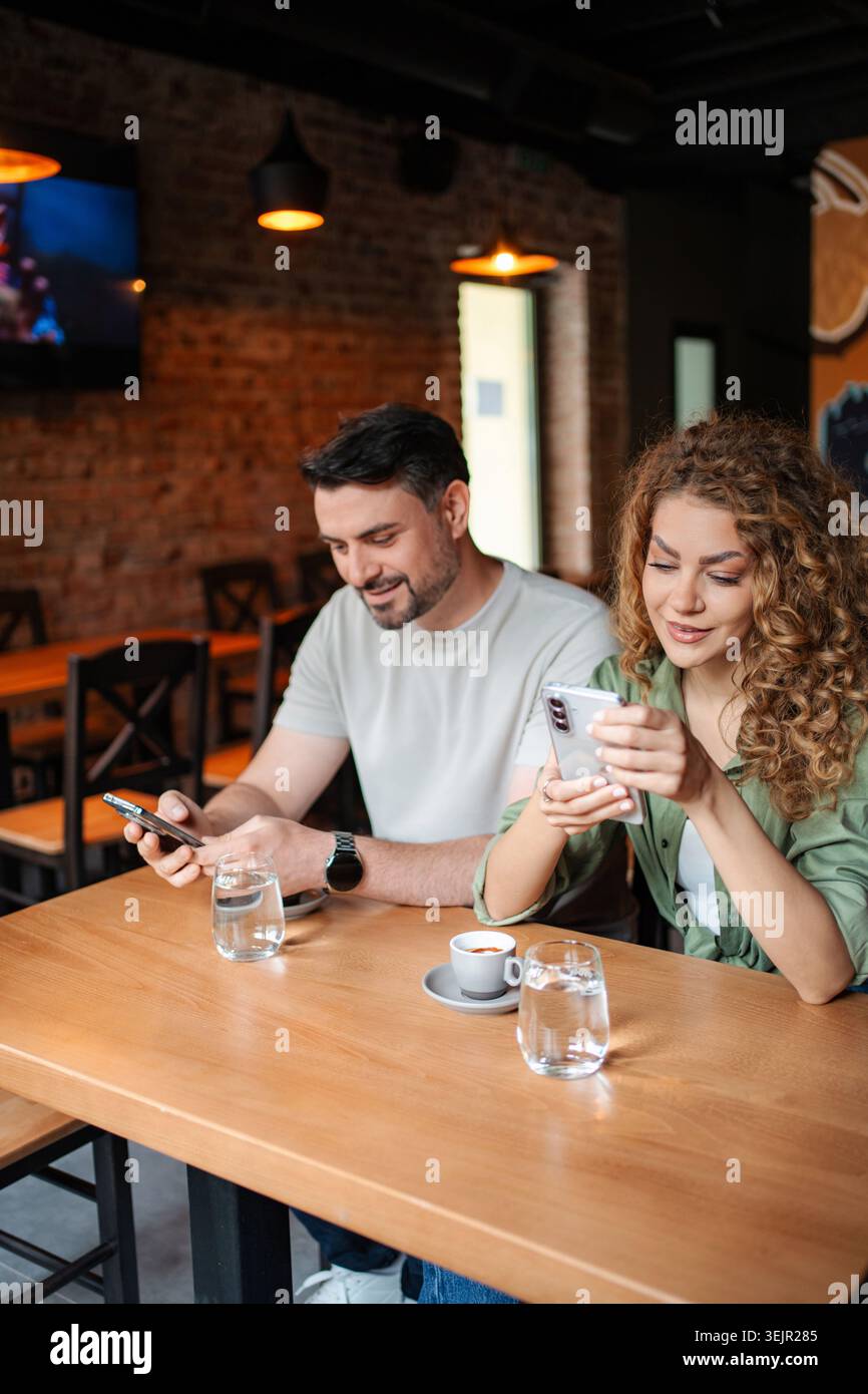 Junges Paar, das Smartphones benutzt, während er Kaffee im Café trinkt Stockfoto