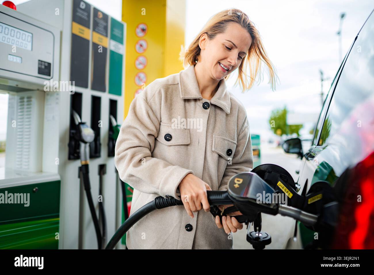 Frau lächelt, die Diesel in ihrem Auto an einer Tankstelle betankt Stockfoto