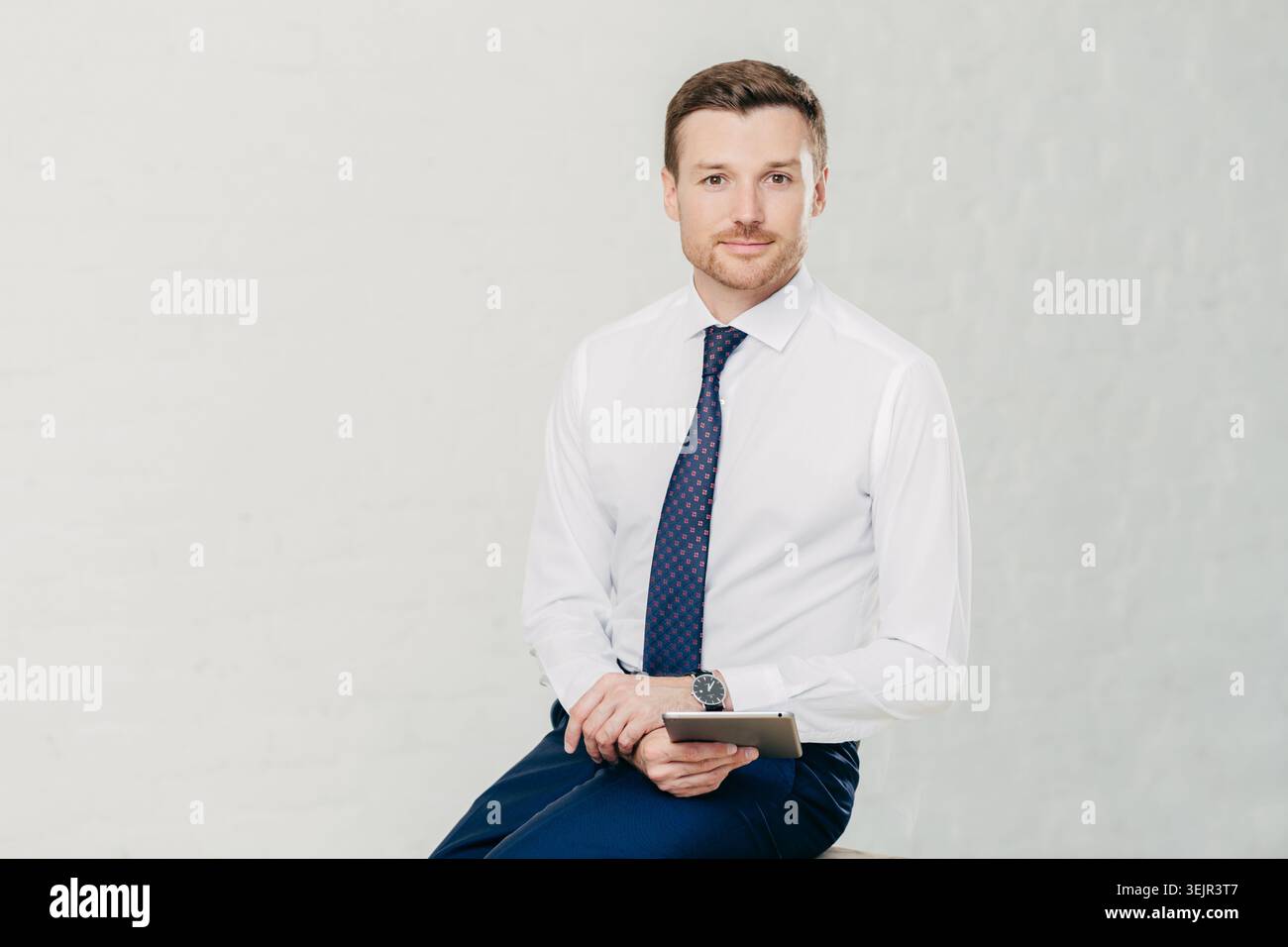 Isolierte Aufnahme eines erfolgreichen männlichen Managers trägt elegantes weißes Hemd, schwarze Hose und Krawatte, verwendet modernen Tablet-Computer für die Arbeit Stockfoto