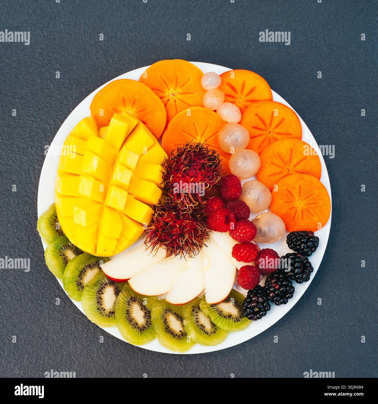 Scheiben reifer exotischer Früchte auf weißem Teller. Kiwi, Mango, Himbeere, Heidelbeere und Persimmon. Obstsortiment. Draufsicht. Heiz Stockfoto