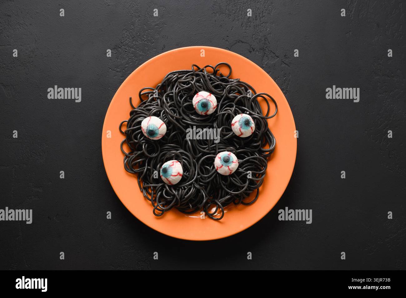 Halloween lustige italienische schwarze Pasta Tintenfisch Tinte verziert Horror Augen in orange Platte mit Rauchtrank auf schwarzem Hintergrund. Horror-Essen für Party. Anzeigen Stockfoto