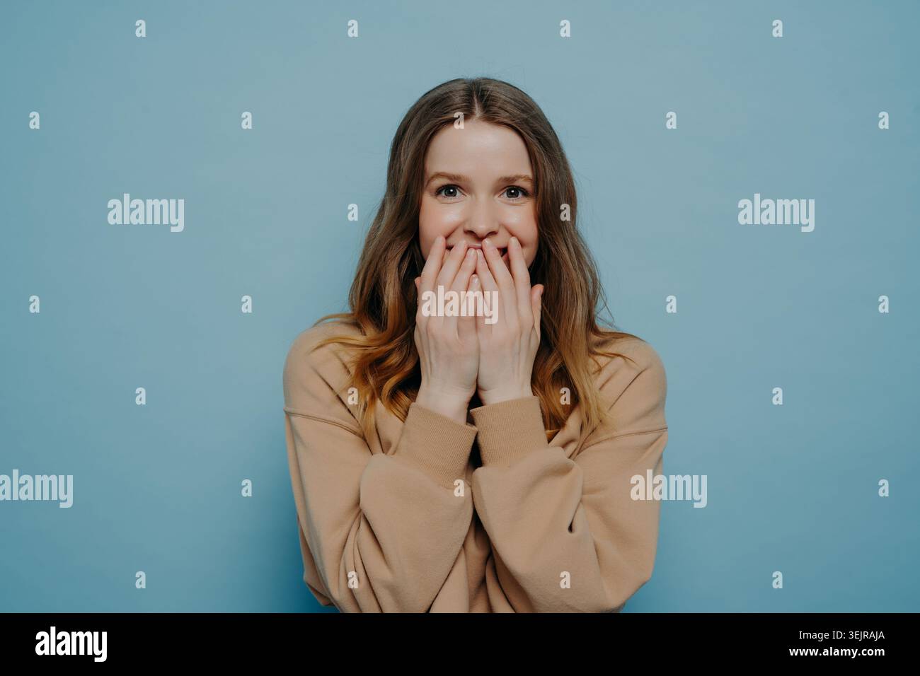 Überraschte junge Frau, die den Mund mit Händen auf blauem Hintergrund bedeckt Stockfoto