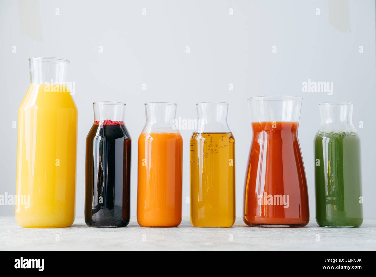 Glasflaschen mit Frucht- und Gemüsesäften in sauberer, minimaler Küche Stockfoto