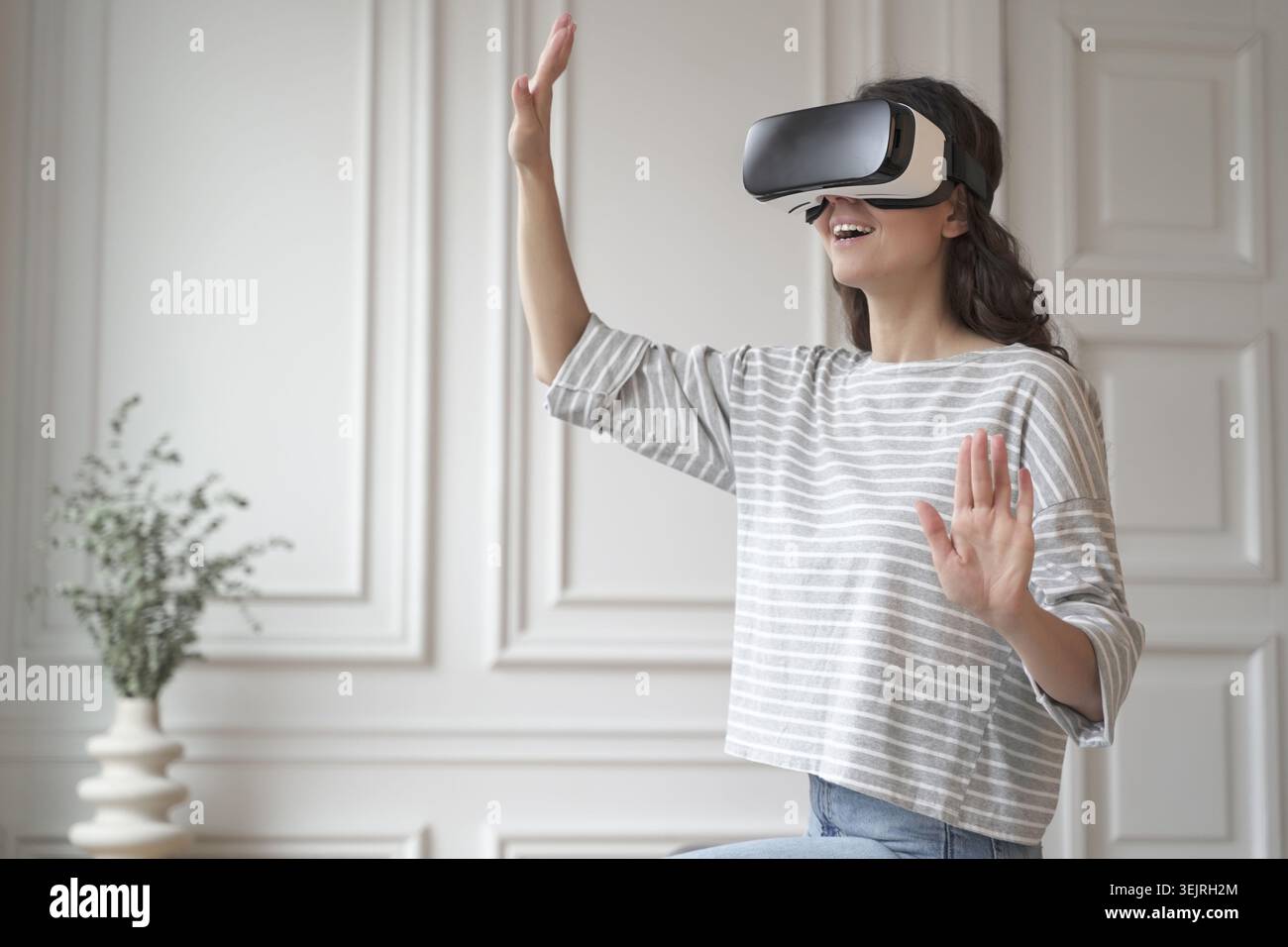 Die junge Frau verwendet Virtual-Reality-Headset und Gesten in hellen, modernen Räumen Stockfoto