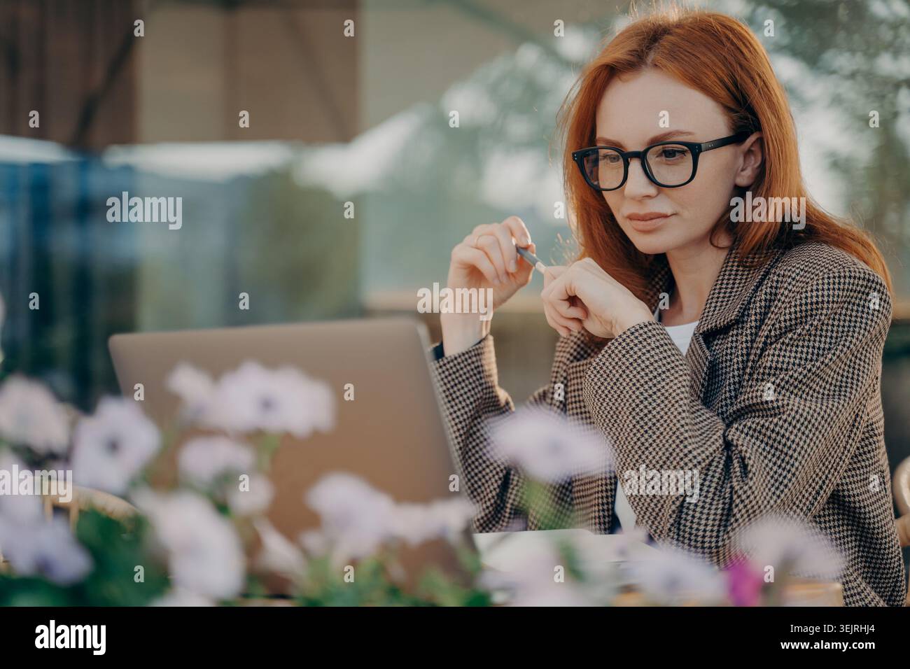 Redhead Geschäftsfrau arbeitet mit Laptop und Stift an einem Tisch im Café mit Blumen Stockfoto