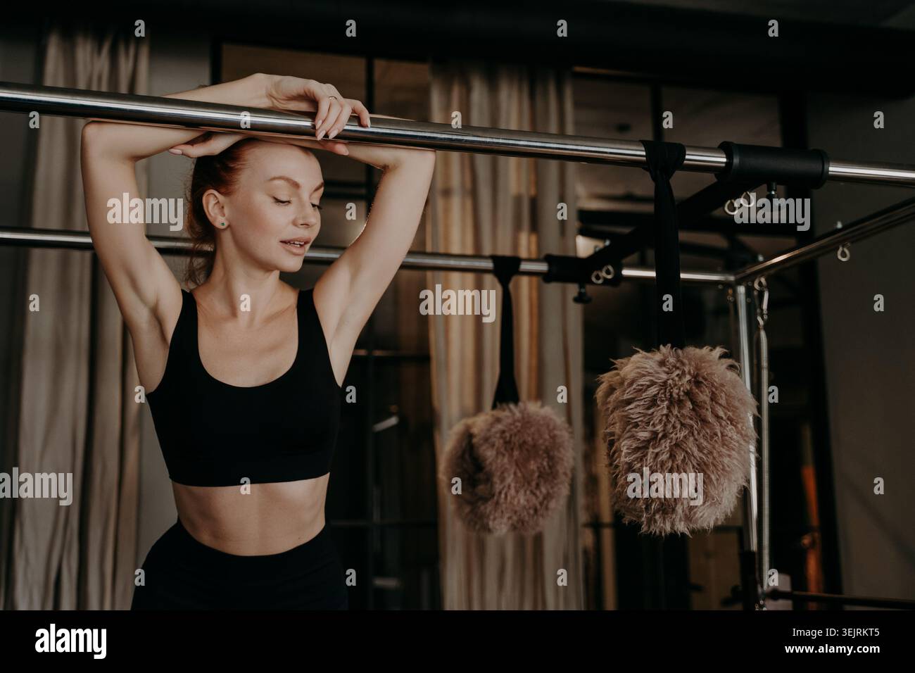 Junge Frau in schwarzer Sportswear, die sich auf Pilates-Reformer-Geräten im Fitness-Studio ausdehnt Stockfoto