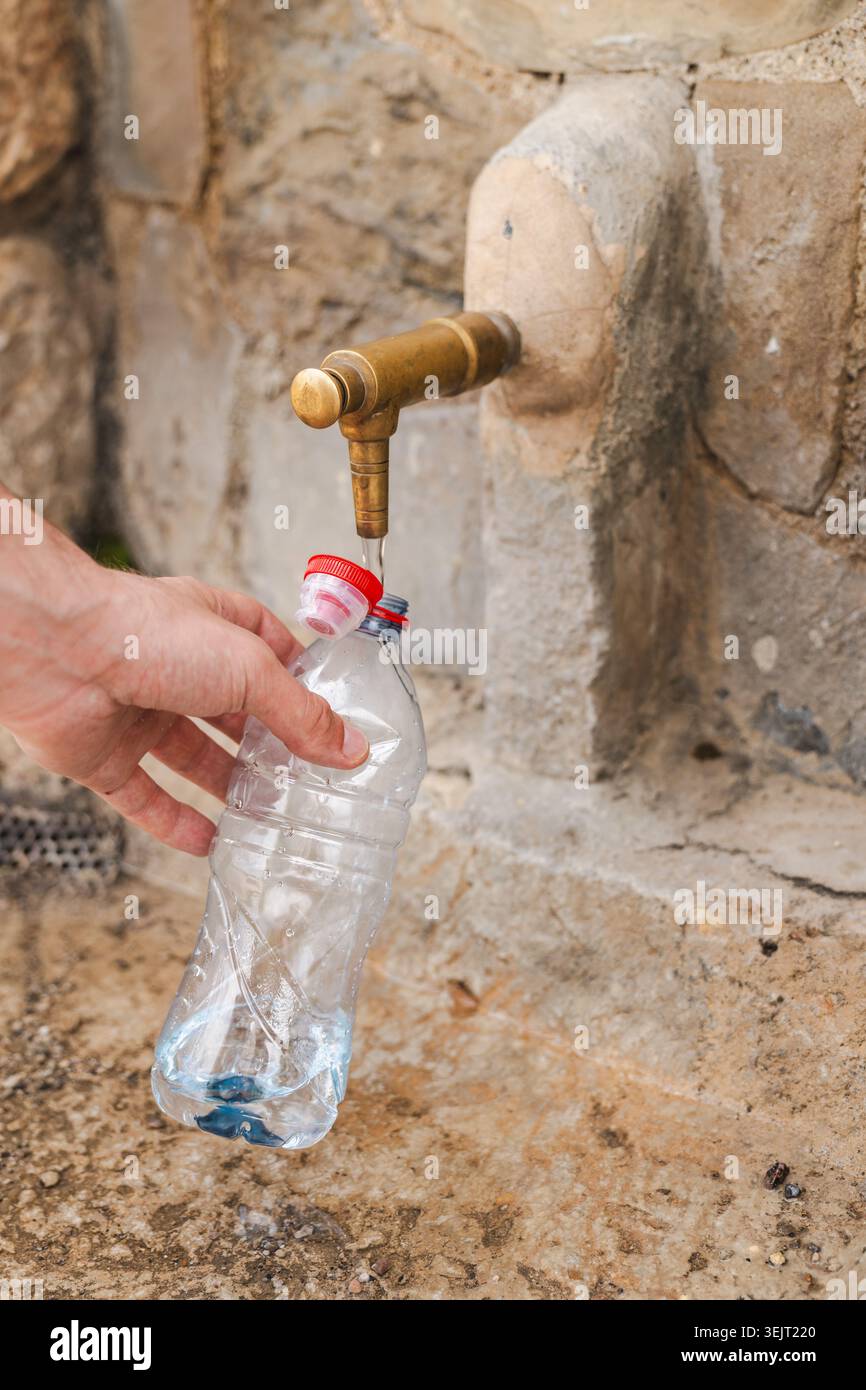 Plastikflasche mit Trinkwasser aus öffentlichem Steinbrunnen von Hand füllen Stockfoto