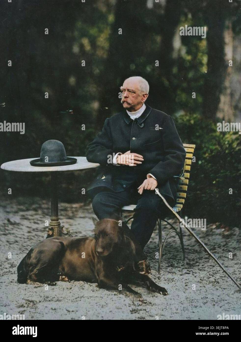Bismarck, 1884. Porträt von Otto von Bismarck an einem Tisch draußen. Er hält einen Stock und seine Mütze liegt auf dem Tisch. Da ruht ein großer schwarzer Hund zu seinen Füßen. (Farbiger Schwarzweiß-Druck). Stockfoto