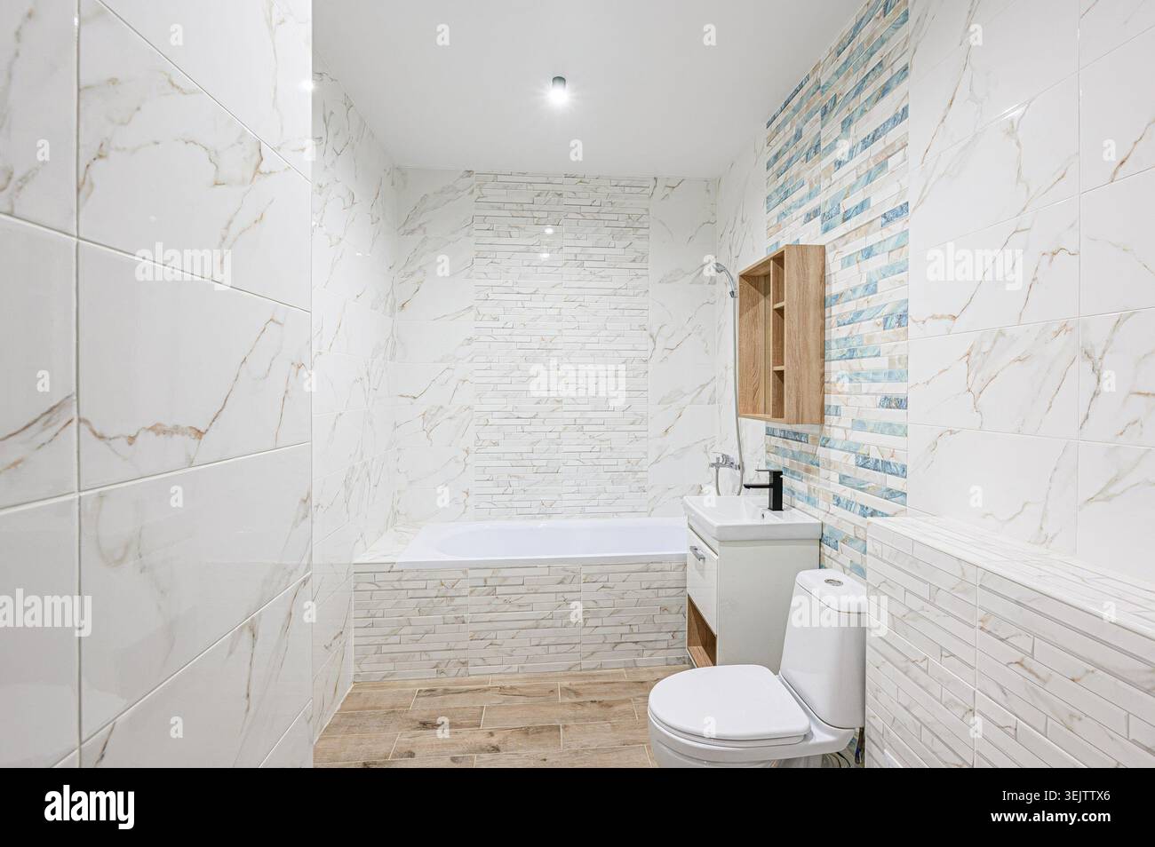 Apartment im Innenbereich modernes, helles Badezimmer mit weißen Marmorfliesen, eingebauter Badewanne, moderner Toilette und Waschbecken. Ein Holzregal sorgt für Wärme Stockfoto