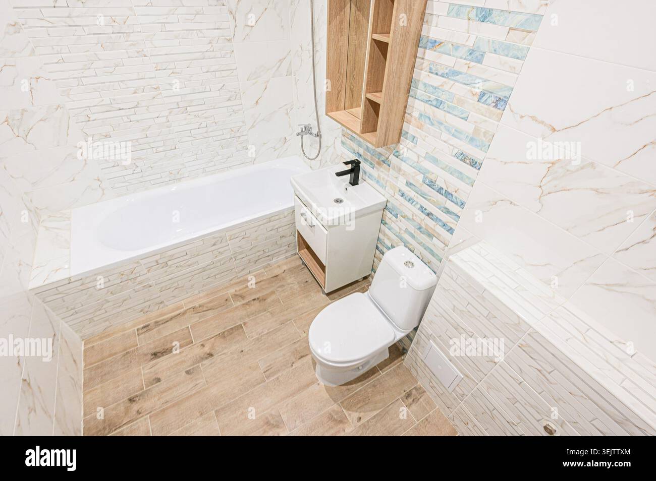 Apartment im Innenbereich modernes, helles Badezimmer mit weißen Marmorfliesen, eingebauter Badewanne, moderner Toilette und Waschbecken. Ein Holzregal sorgt für Wärme Stockfoto