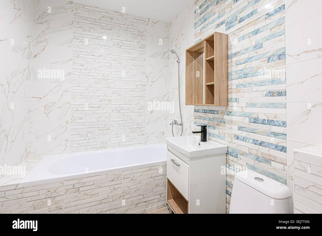 Apartment im Innenbereich modernes, helles Badezimmer mit weißen Marmorfliesen, eingebauter Badewanne, moderner Toilette und Waschbecken. Ein Holzregal sorgt für Wärme Stockfoto