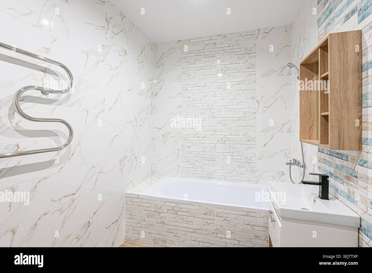 Apartment im Innenbereich modernes, helles Badezimmer mit weißen Marmorfliesen, eingebauter Badewanne, moderner Toilette und Waschbecken. Ein Holzregal sorgt für Wärme Stockfoto