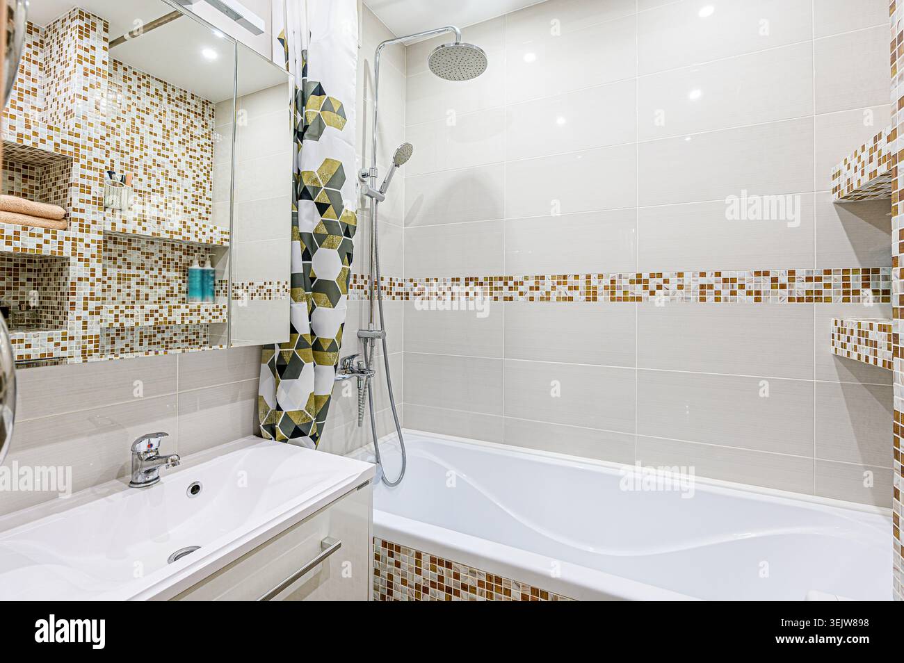 Modernes Bad mit Mosaikfliesen, weißer Badewanne und eleganter Dusche. Der Raum verfügt über eingebaute Regale und eine geometrische Duschkabine Stockfoto