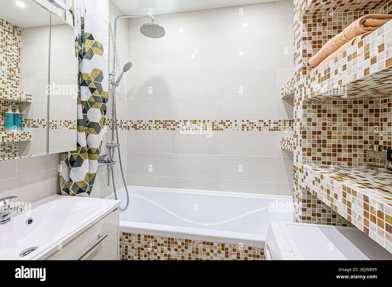 Modernes Bad mit Mosaikfliesen, weißer Badewanne und eleganter Dusche. Der Raum verfügt über eingebaute Regale und eine geometrische Duschkabine Stockfoto