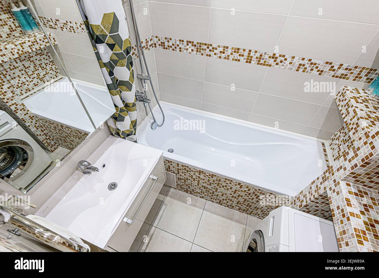 Modernes Bad mit Mosaikfliesen, weißer Badewanne und eleganter Dusche. Der Raum verfügt über eingebaute Regale und eine geometrische Duschkabine Stockfoto
