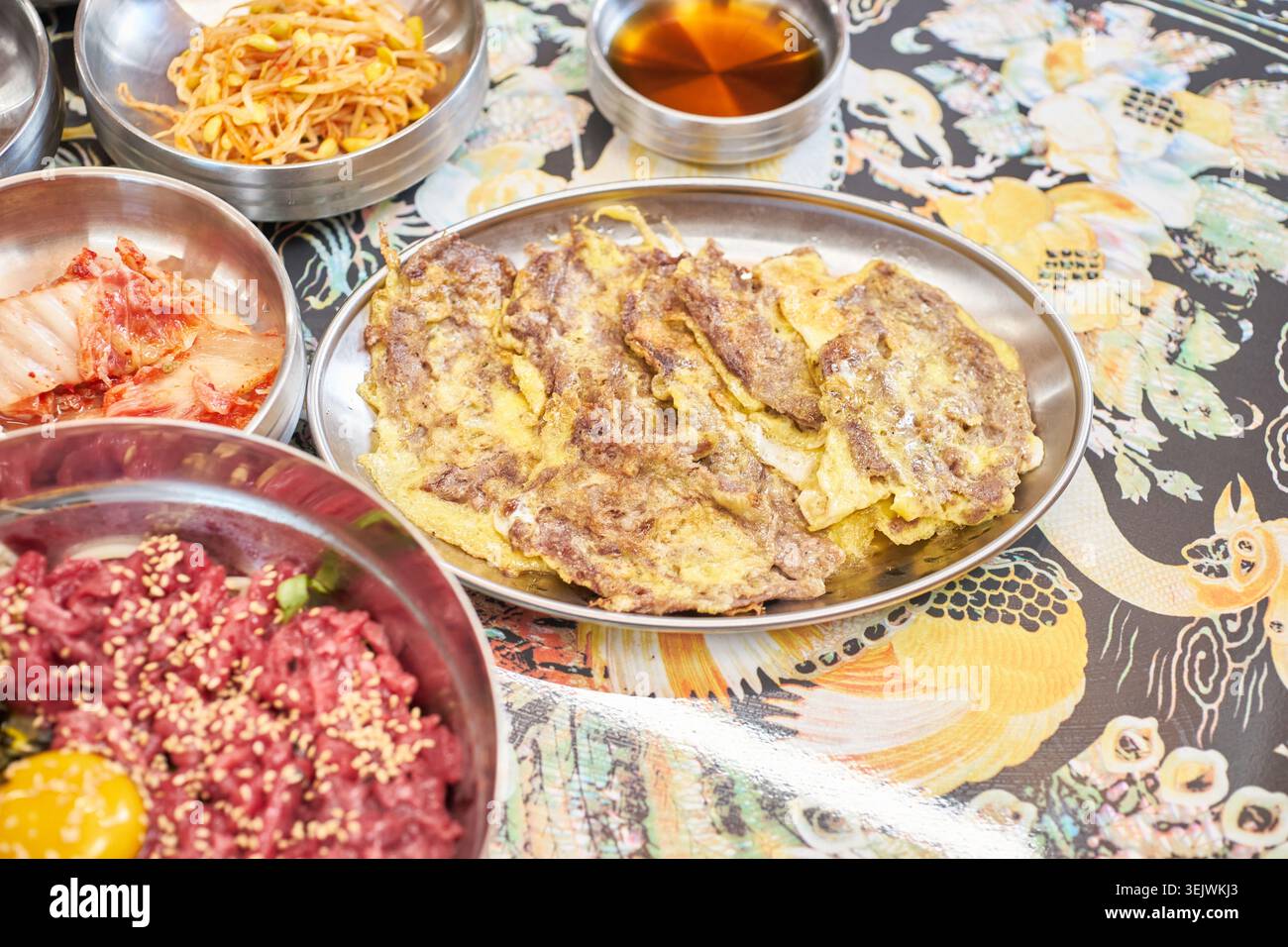 Genießen Sie eine luxuriöse koreanische Mahlzeit mit frischem rohem Rindfleisch-Bibimbap und herzhaftem, in der Pfanne gebratenem Rindfleisch. Diese Kombination bietet eine perfekte kulinarische Harmonie. Stockfoto